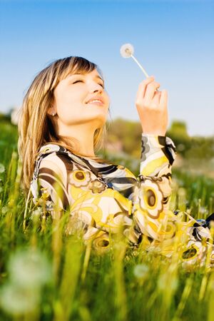 Attractive young girl relaxing on a meadow, holding dandelion flower in her handの写真素材