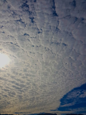 Celestial Canvas: A bright blue sky speckled with white clouds, illuminated by the radiant glow of...