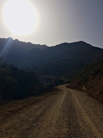 A gravel road winds through high mountains in the early morning, while the sun still crowns the peaks.の写真素材