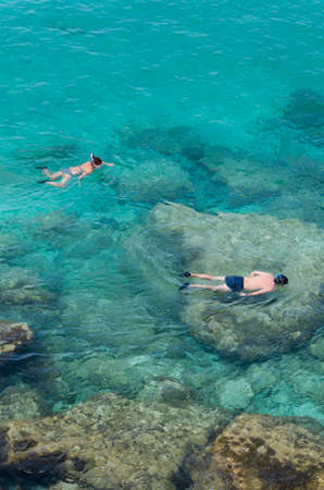 Two people do snorkeling near the rocks in a wonderful blue and green sea