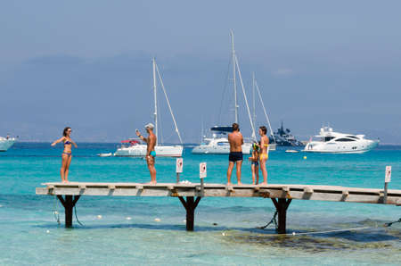 Formenreta, Spain, Plaja de ses Illetes - July 20, 2015: Some people during the holidays intent to photograph on a pier, in the background Speedboats moored in a sea blue and greenのeditorial素材
