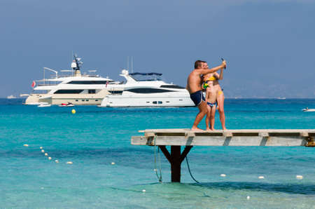 Formentera, Spain, Plaja de ses Illetes - July 20, 2015: Family during the holidays makes selfie on a pier, in the background Speedboats moored in a sea blue and greenのeditorial素材