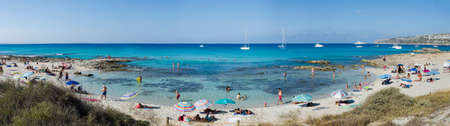 Formentera, Spain, Calo de Sant August- July 23, 2015: View on the beach, many people with their umbrellas, against the backdrop of the blue and green sea, boats moored offのeditorial素材