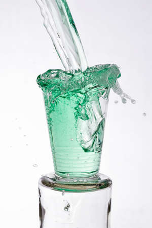 Green drinks poured vigorously overflowing splashing from a glass, on a white backgroundの写真素材