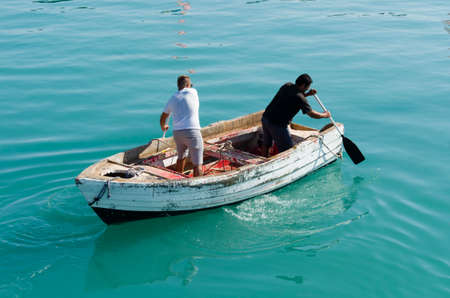 Zakynthos, Greece, July 15, 2016: Two men row in the opposite direction on an old wooden boat...
