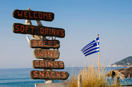 Wooden signposts on the beach indicate the presence of a bar offering food and drink in Skiathos, Greece, on the bottom the Greek flagの写真素材