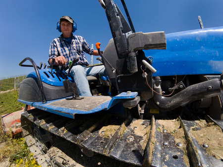 Driver on crawler tractor with noise-free headphones works in the vineyard in the Langhe hills in Piedmont Italyの写真素材