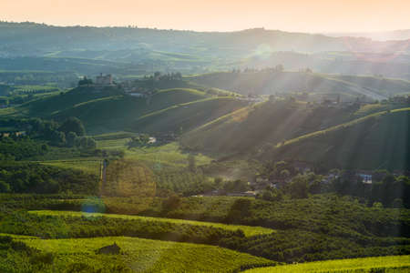 View on the langhe hills and castle of Grinzane cavour at Sunset, the sky is yellow and orange and some sunrays illuminate the Manor in backlightのeditorial素材