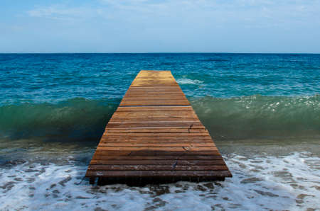Wooden pier on the infinite sea without anyone, under it passes a wave that breaks on the shore