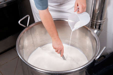 Cheesemaker pours the rennet with a ladle and a jugの写真素材