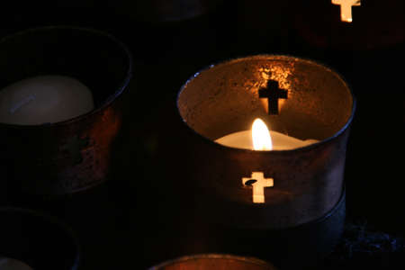 small votive candles burning in religious cups with cross cutoutsの写真素材