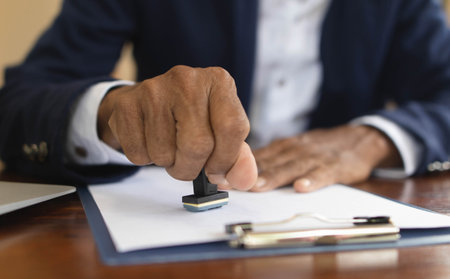 Close-up of a person's hand stamping on an approved application form and approved contract form on...