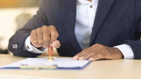 Business man person's hand stamping with approved stamp on certificate document public paper at desk, signing on business partner paper to success, or concept of attorney and insuranceの写真素材