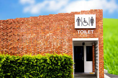 The red brick public restroom with symbols for men, women and people with disabilities is designed for a universal design against a backdrop of blue sky and white clouds.の写真素材
