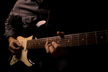 Guitarist holding electric guitar in hand and strumming chord on black background.