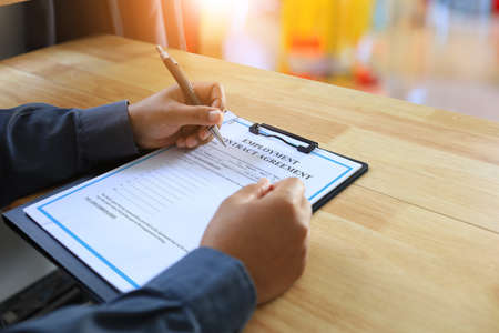 An employee is signing an employment contract to be aware of the employment agreement and the regulations of the company employee on the wooden desk in the office.の写真素材