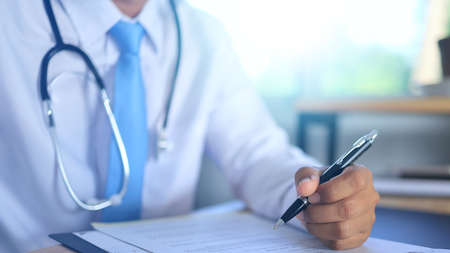 A male doctor dressed in white writing a patient's medical history during the day at the hospital.の写真素材