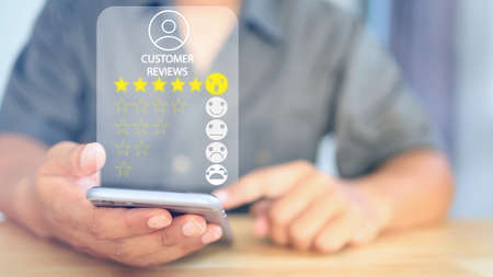 Close up on customer hand pressing on smartphone screen with give five star rating feedback and excellent level ranking to service companies, business concept.の写真素材