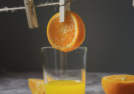 Closeup shot of oranges hanging on a string rope are dripping onto the glass, giving a fresh and...