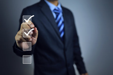 Businessman using pen to tick correct sign or check mark on checkbox to complete task and things to do checklist in document control syetem. Project approve and done concept.の写真素材