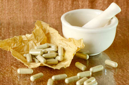 Herbal medicine grinder and filled capsule on brown papers の写真素材