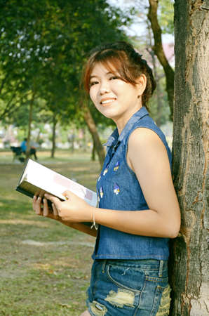 Portrait of young beautiful Asian woman reading a book in the garden under warm sunlight in the morning の写真素材