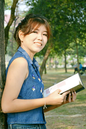 Portrait of young beautiful Asian woman reading a book in the garden under warm sunlight in the morning の写真素材