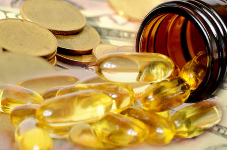 Soft gelatin dietary supplement oil capsule and money in drug expense concept の写真素材