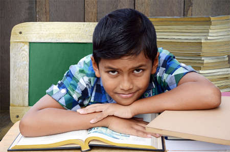 Asian boy in the classroom with Stack of Old Books and Blackboard on Wood Background in Oldies Education Concept.の写真素材