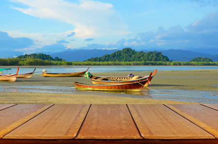 Outdoor Picnic Background with Wooden Table in Afternoon Light with Landed Folk Fishing Boat at Bang Ben Beach in Ranong, Thailand.の写真素材