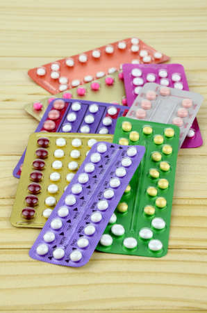 Colorful oral contraceptive pill strips on pine wood table.の写真素材