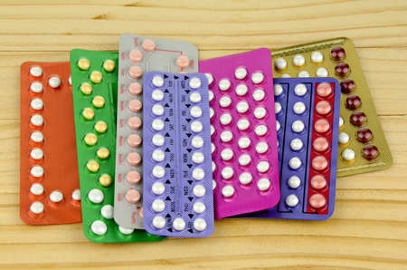 Colorful oral contraceptive pill strips on pine wood table.の写真素材