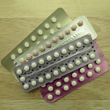 Colorful oral contraceptive pill strips on pine wood table.の写真素材