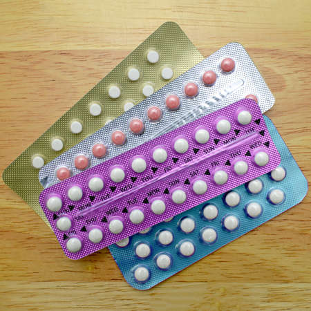 Colorful oral contraceptive pill strips on pine wood table.の写真素材