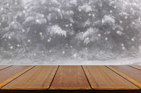 Blurred snowing in pine forest through glass window background with wood table.の写真素材