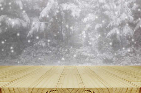 Blurred snowing in pine forest through glass window background with wood table.の写真素材
