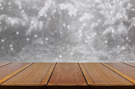 Blurred snowing in pine forest through glass window background with wood table.の写真素材