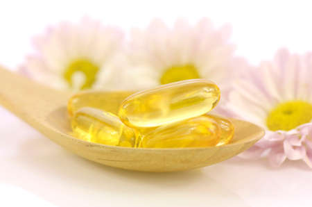 Soft gelatin capsules of dietary supplement with chrysanthemum flowers background in warm light tone represented women health concept.の写真素材