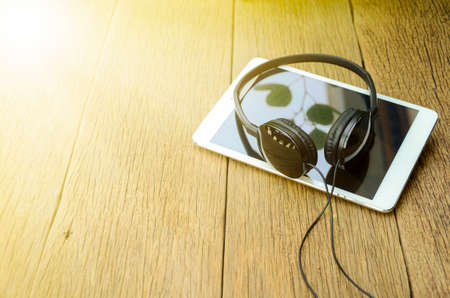 Head phone and computer tablet on old wood table background in soft and warm light tone.の写真素材