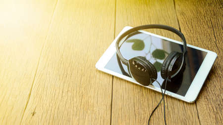 Head phone and computer tablet on old wood table background in soft and warm light tone.の写真素材