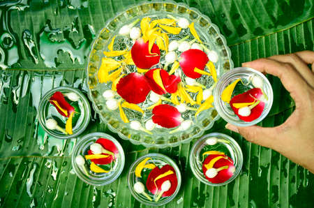 Banana leaves as background with wood blow fill with fragrant water, rose petals, marigold petals and jasmine flowers. Songkran festival inThai style background.の写真素材