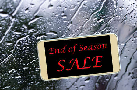 End of season sale sign on glass window with rain drops.