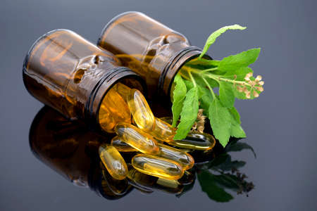 Oil in capsule, amber bottle and fresh herbs on dark background in traditional medicine concept.の写真素材