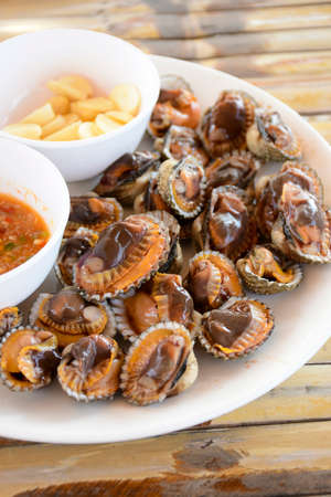 Parboiled cockles or bloody cockles with spicy Thai style dip sauce and garlic on bamboo table background.の写真素材