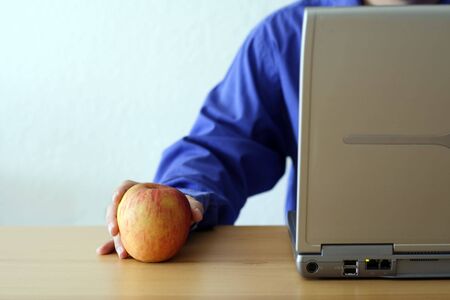 Businessman working on a laptop and holding an appleの写真素材