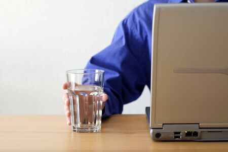 A businessman working on a laptop and holding a glass of waterの写真素材