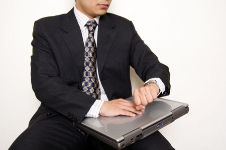 A businessman looking at his watch while holding a laptop, can be used for deadline/waiting metaphorの写真素材