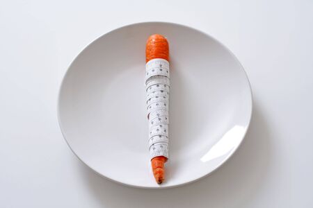Carrot wrapped with measuring tape on a plateの写真素材