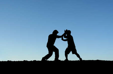 Two men practicing martial arts on top of a mountain (in silhouette)の写真素材