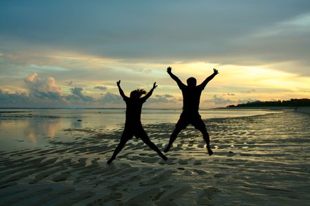 Two people in silhouette jumping happily on a beach